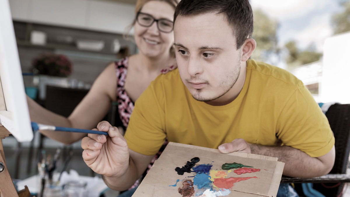 A person with disabilities is painting a picture with paintbrush and palette in hand.