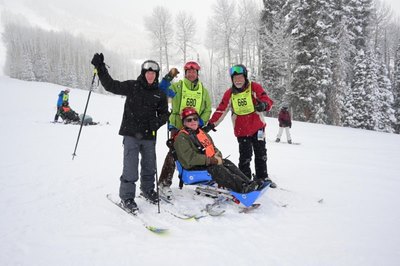 Four people gathered with ski equipment on a snowy mountainside.